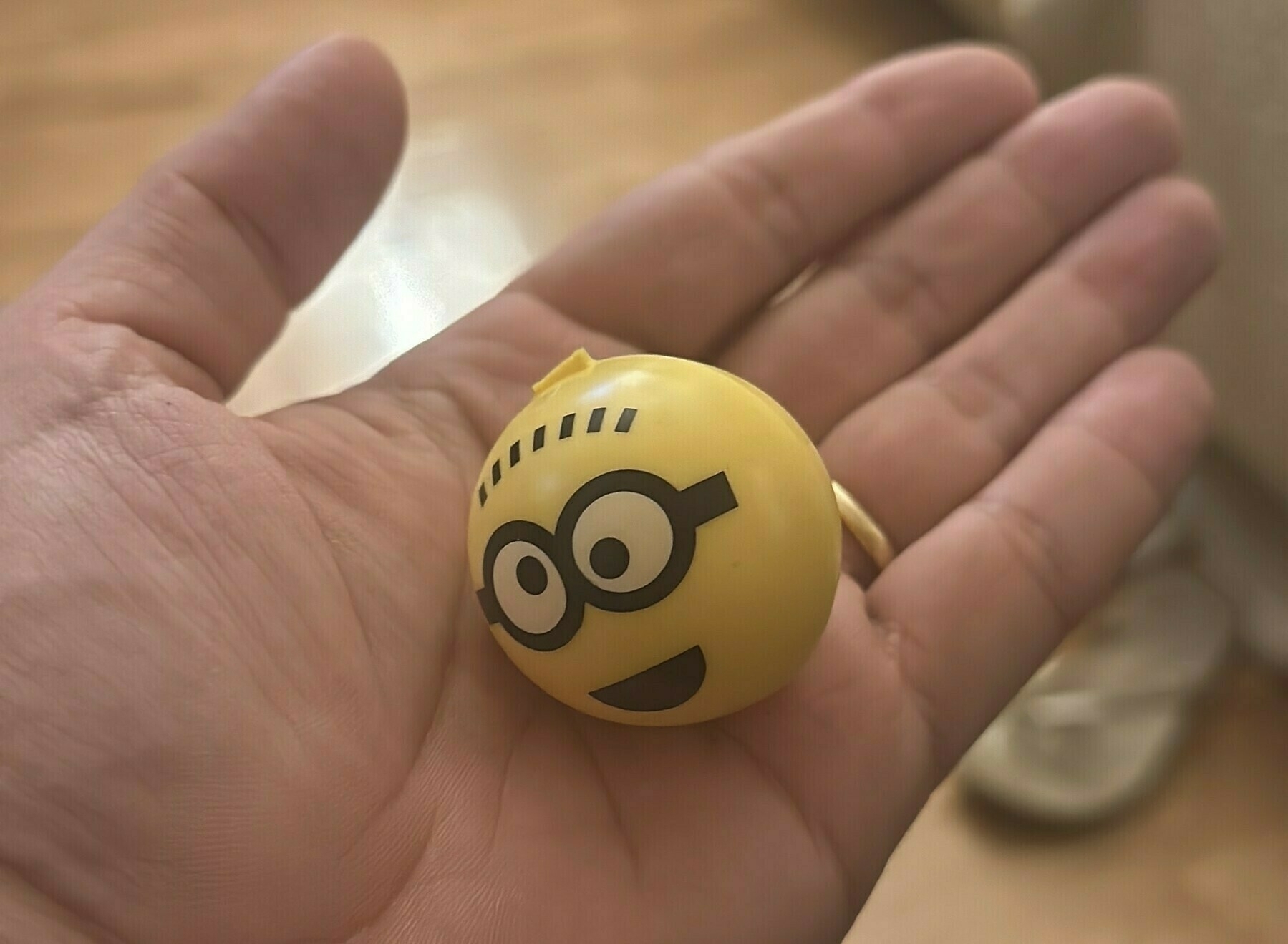 A hand holds a yellow ball with a cartoon Minion face
