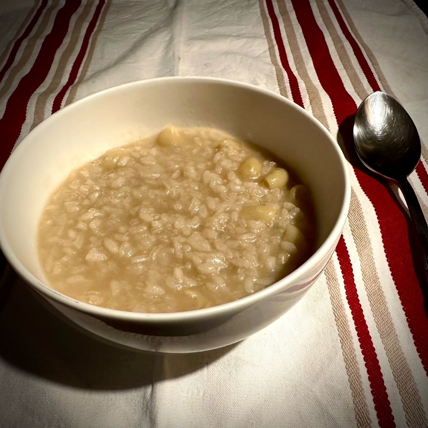 A bowl of risotto rests on a striped tablecloth with a spoon to the side.