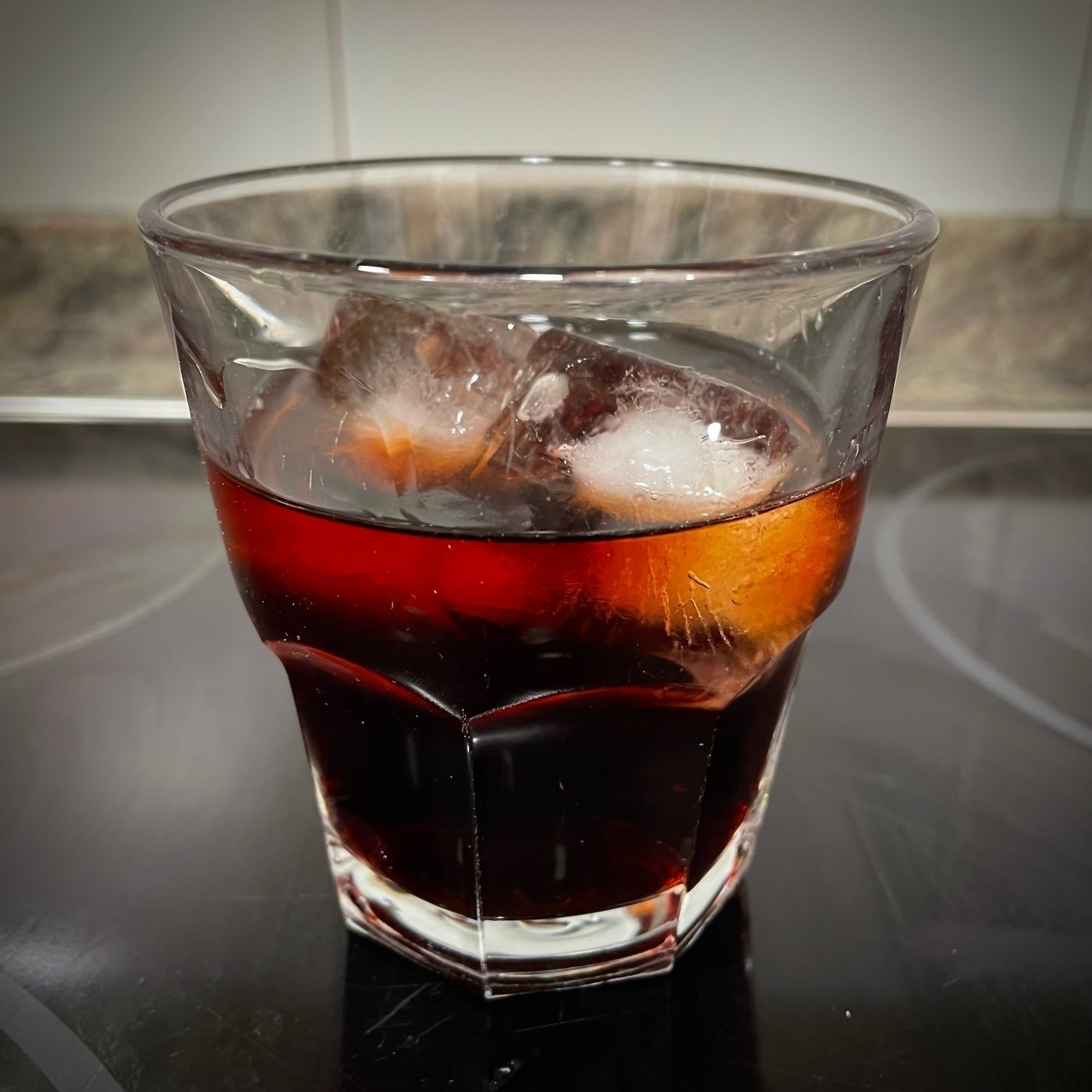 A Negroni with ice sits in a short glass on a reflective surface.
Spanish: Un Negroni con hielo está en un vaso bajo sobre una superficie reflectante.
Basque: Negroni bat izotzekin edalontzi batean dago, islatzen duen gainazal batean.