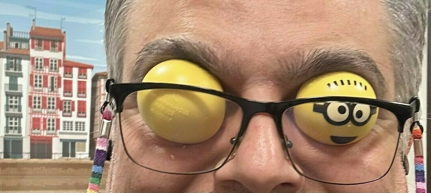 A person wears glasses with lenses replaced by images of cartoonish yellow eyes against an urban backdrop.
Spanish: Una persona lleva gafas con lentes reemplazadas por imágenes de ojos amarillos caricaturescos sobre un fondo urbano.
Basque: Pertsona batek hiri-atzeko fondeo batean marrazki bizidunetako begi hori irudiekin ordezkatutako lenteak dituzten betaurrekoak janzten ditu.