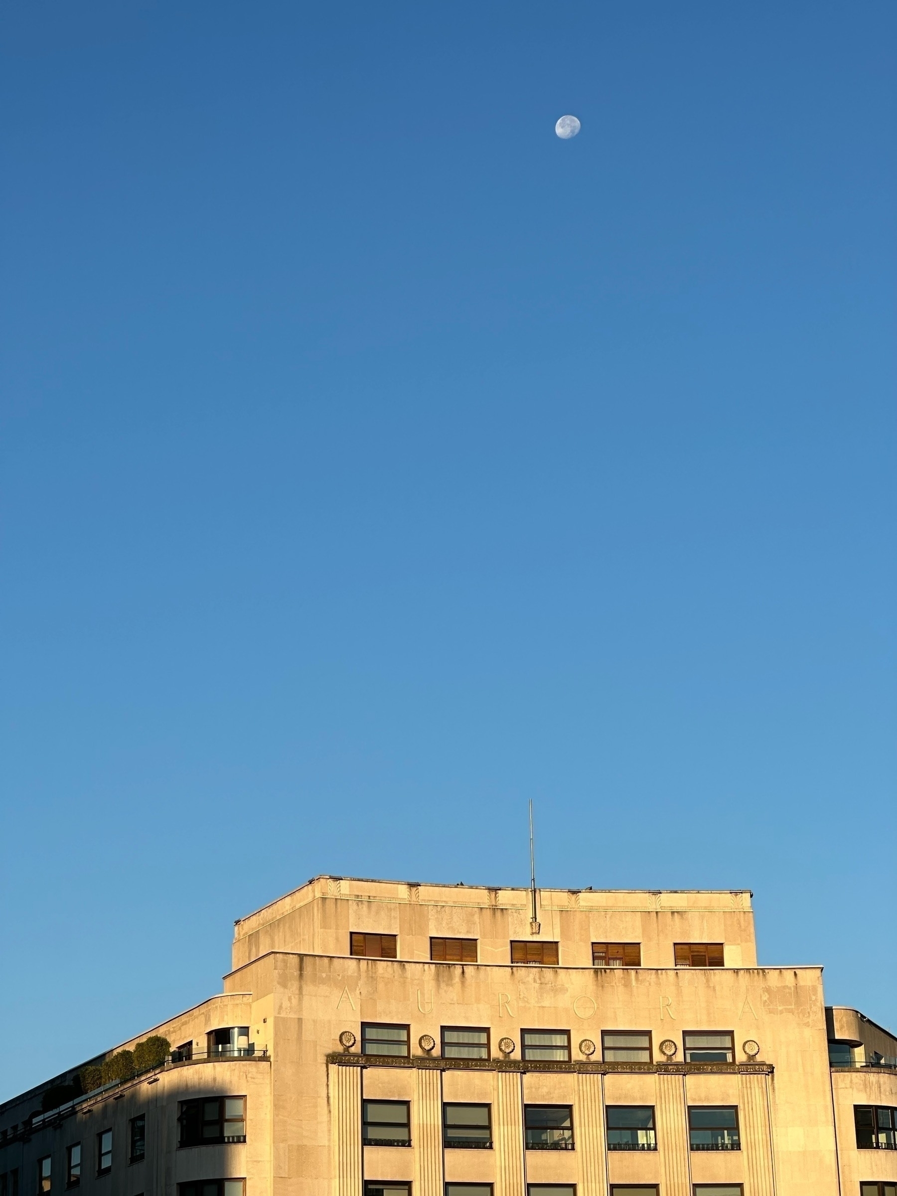 A waxing gibbous moon floats above an art deco building against a clear blue sky during twilight.
Spanish: Una luna gibosa creciente flota sobre un edificio art deco contra un cielo azul claro durante el crepúsculo.
Basque: Ilargi gibosoa hazten ari dena flotatzen dago art deco eraikin baten gainean zeru urdin argiaren kontra ilunabarrean.