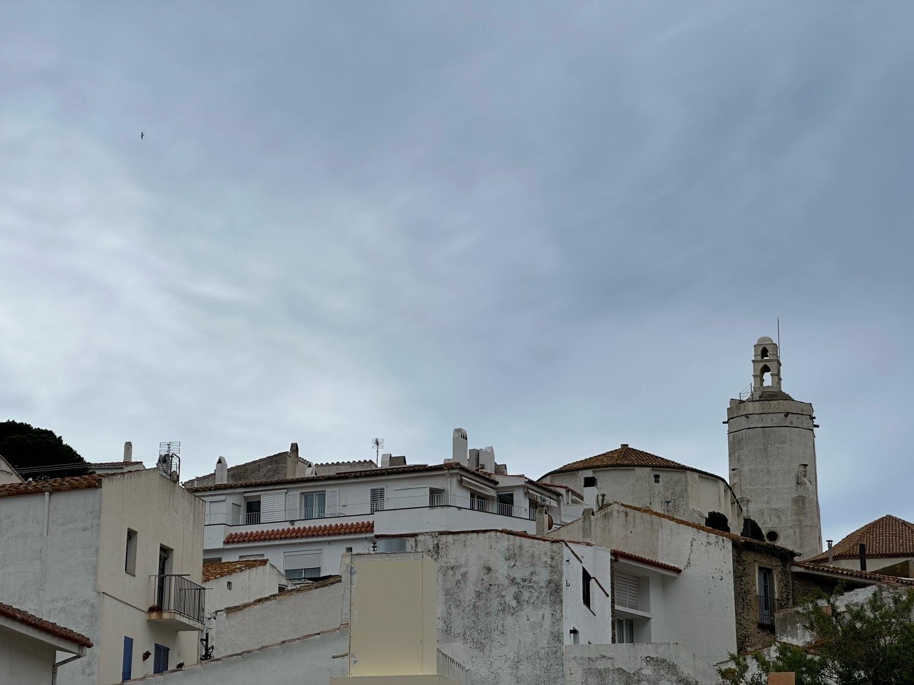 White buildings with varied rooftops under a cloudy sky, one building with a bell tower stands out.
Spanish: Edificios blancos con tejados variados bajo un cielo nublado, uno con campanario destaca.
Basque: Zeru lainotsu baten azpian dauden teilatu desberdineko eraikin zuriak, kanpandorre bat duen eraikin bat nabarmentzen da.